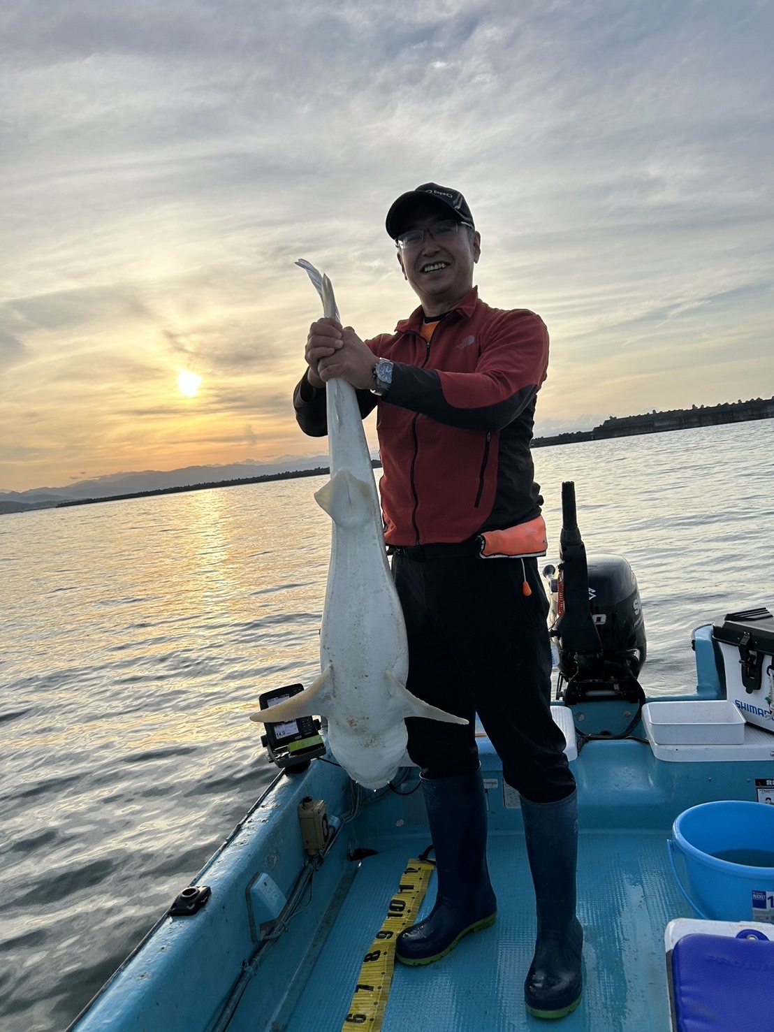 夕日の海で釣った魚を持つ松本さん